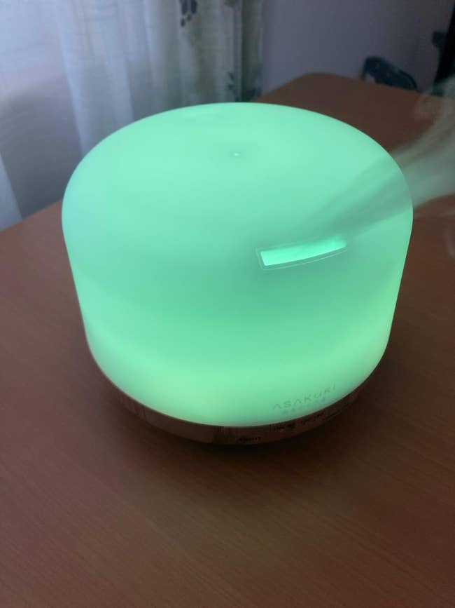 A glowing greenish indispensable lipid diffuser releasing mist connected a woody table