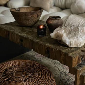 A rustic wooden coffee table featuring a candle, wooden bowls, and a large crystal cluster, placed in a cozy living space with a woven basket nearby