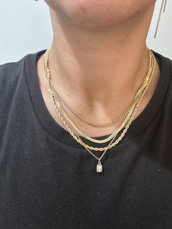 Person wearing layered golden necklaces with varying concatenation styles and a pendant, implicit a plain acheronian top