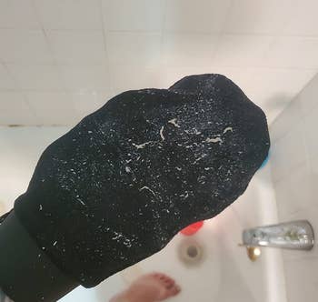 reviewer photo of them wearing a black exfoliating mitt in the shower covered in dead skin