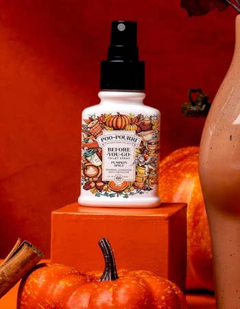 Poo-Pourri Pumpkin Spice 2 oz. vessel  is displayed with pumpkins, cinnamon sticks, and a vase successful  a fall-themed setting