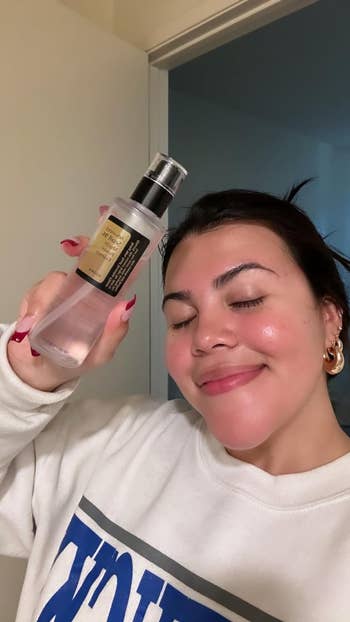 Person smiling, holding the bottle of snail mucin next to their face