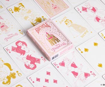 Disney Princess-themed playing cards with characters similar  Ariel and Belle, packaged successful  a decorative box, are arranged connected  a table