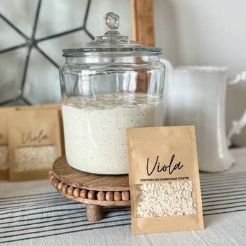 Glass jar of sourdough starter connected  a woody  stand, with a packet labeled 