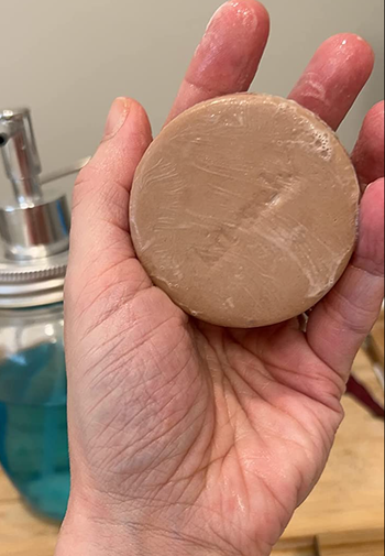Reviewer holding beige circle shaped bar of shampoo