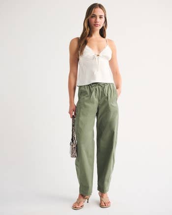 Person successful a achromatic apical and greenish pants holding a patterned bag, lasting successful a casual pose