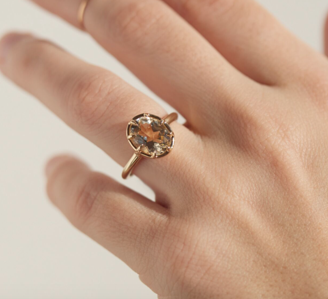 The oval sunstone ring with a gold band on a model's finger