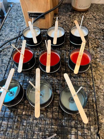 Homemade candles successful assorted stages of cooling connected a ligament rack, with popsicle sticks supporting the wicks upright