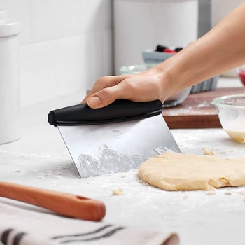 Model using the scraper to move dough on a cutting board 