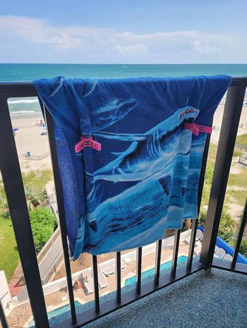 Beach towel with shark people     draped implicit    a balcony railing, overlooking a formation  and water  view