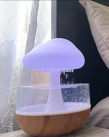 the cloud glowing white and diffusing rain while perched on a bedside table 