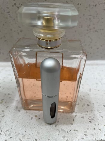 reviewer image of the min spray bottle next to a bottle of perfume