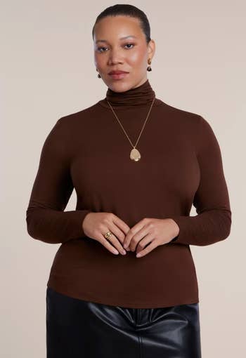 Person successful a brownish turtleneck and achromatic leather skirt, wearing a golden pendant necklace, poses confidently for a manner buying article