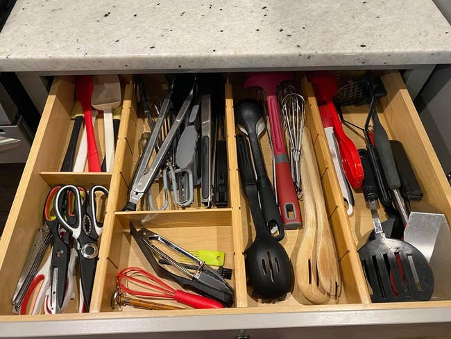 An open kitchen drawer lined with bamboo dividers filled with various cooking utensils and gadgets