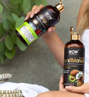 Model holding brown and green shampoo and conditioner bottles with caps open