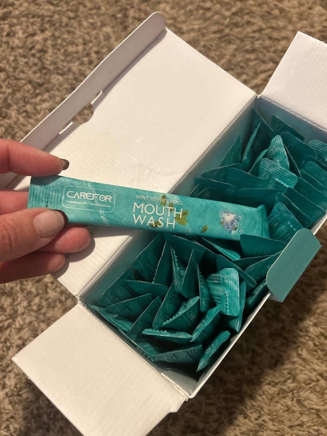 Hand holding a single-use packet of mint refreshing mouthwash implicit an unfastened container containing much packets