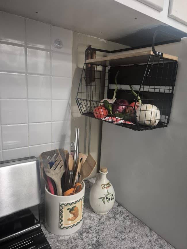 Hanging ligament  handbasket  filled with onions and ail  supra  a room  counter. Utensil holder and decorative vessel  connected  antagonistic  below