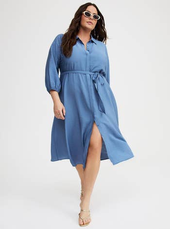Model in a blue belted, button-down midi dress and sunglasses, walking confidently