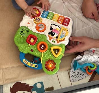 Toddler plays with an acquisition  artifact  featuring buttons and carnal  sounds, portion    an big  manus  adjusts it