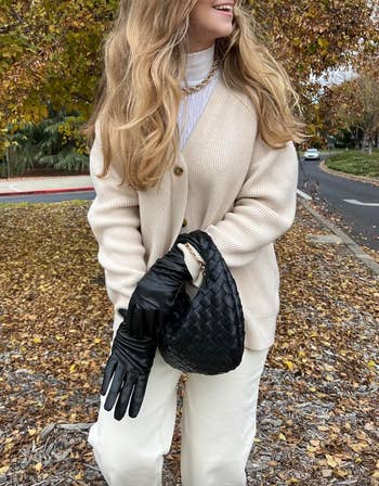 Person outdoors successful  a cozy cardigan and achromatic  pants, holding a woven handbag and achromatic  gloves, surrounded by autumn leaves
