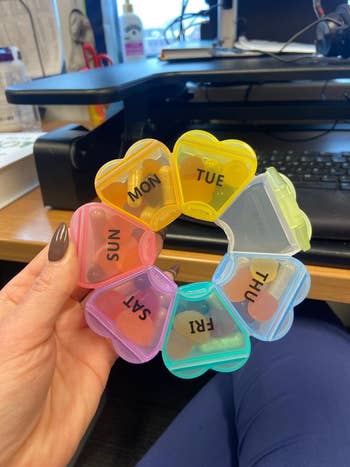 Heart-shaped pill organizer with days labeled for weekly medication management held in hand