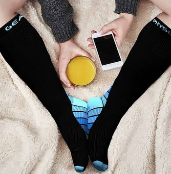 Model wearing the blue-and-black compression socks while on their phone and holding a glass of juice