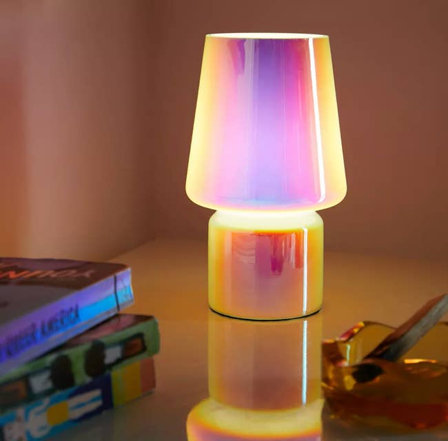 A modern, gradient glass lamp emits warm light on a table, surrounded by books and a decorative disco ball on a nearby shelf