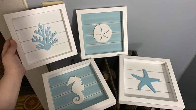 reviewer photo of the four blue and white wall decor pieces, which picture a starfish, seahorse, sand dollar, and coral