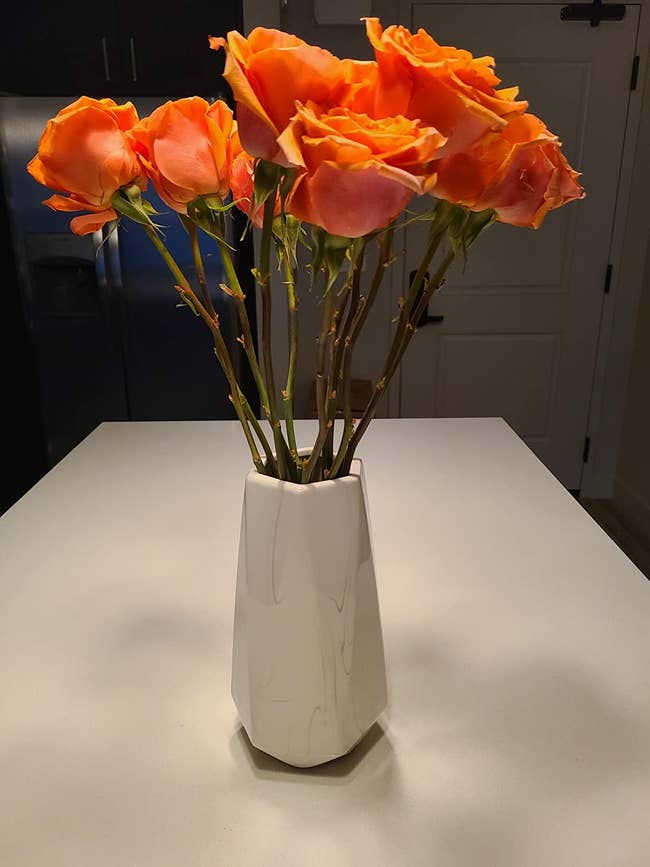 Reviewer image of white marble vase with rounded edges and orange roses inside on top of white table