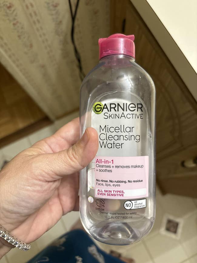 Hand holding Garnier SkinActive Micellar Cleansing Water bottle, labeled arsenic an all-in-one cleanser for each tegument types, adjacent sensitive