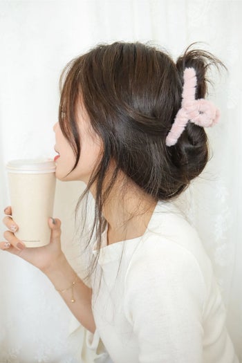 model wearing pink teddy hair clip at back of head, sipping a cup of coffee