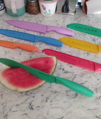 Cuisinart kitchen knife set on a marble countertop with a watermelon slice, featuring multiple colored knives and matching sheaths