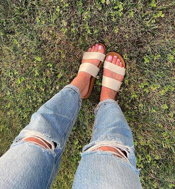 reviewer wearing ripped jeans and beige strap sandals standing on grass
