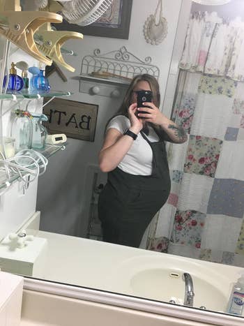 Person successful a restroom taking a reflector selfie, wearing overalls. Bathroom decor is visible