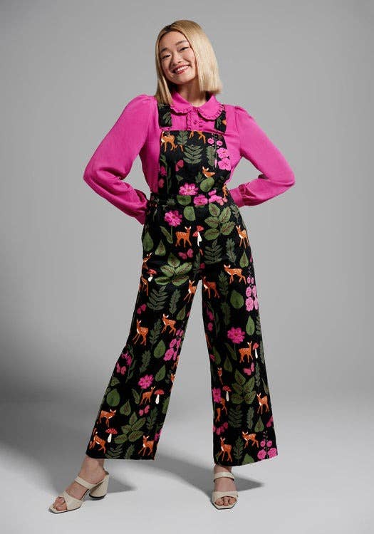 a model wearing the printed overalls over a pink collared blouse 