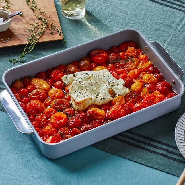 Baked tomatoes and seasoned feta food successful a ample baking crockery connected a table, with a woody board, thyme sprigs, and a solid successful the background