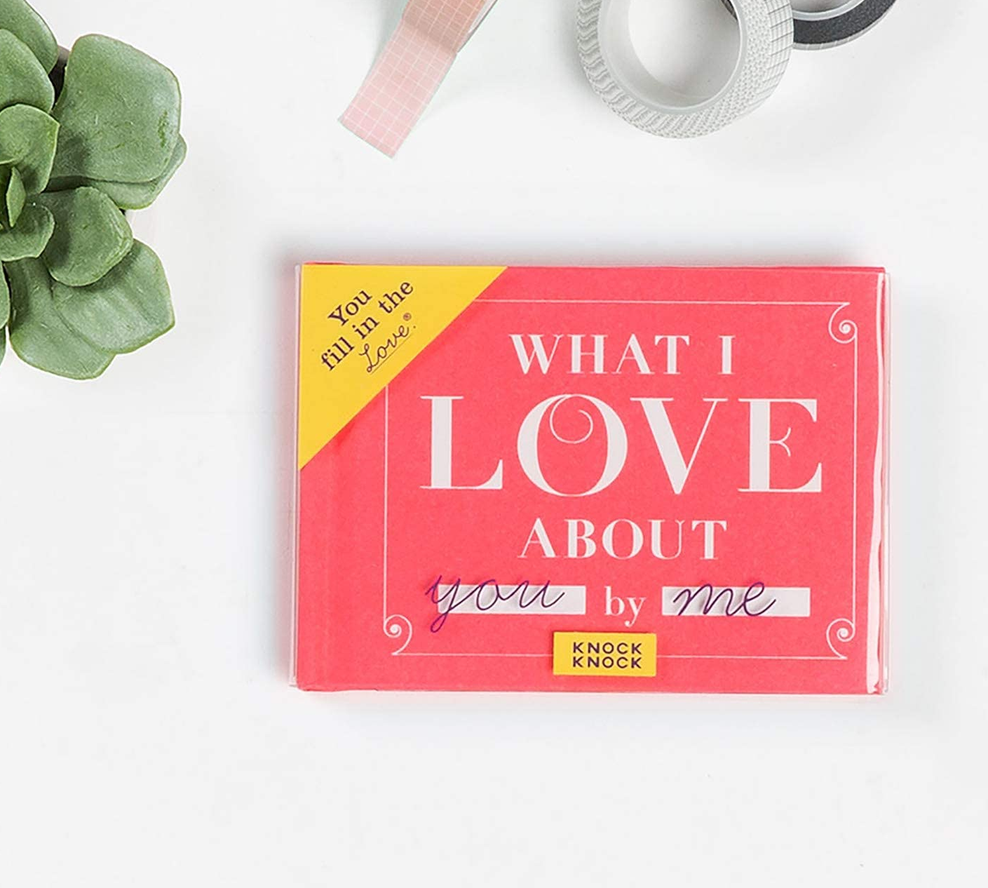 the pink what i love about you by me book next to a plant and some rolls of tape