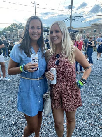 Two women smiling, holding drinks, at an outdoor event in casual dresses