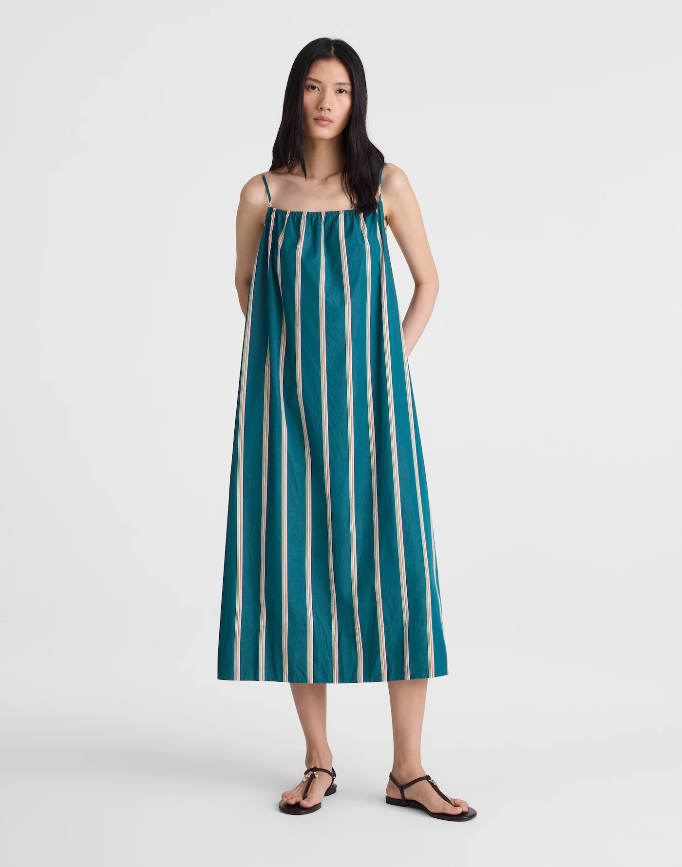 Model in a loose, green striped maxi dress and sandals stands against a plain background