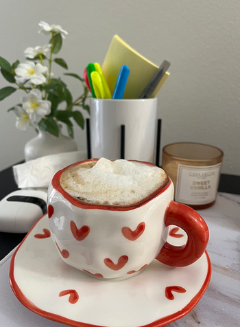A white mug and plate with squiggly shaped red-lined edges and little red painted hearts patterend on it 