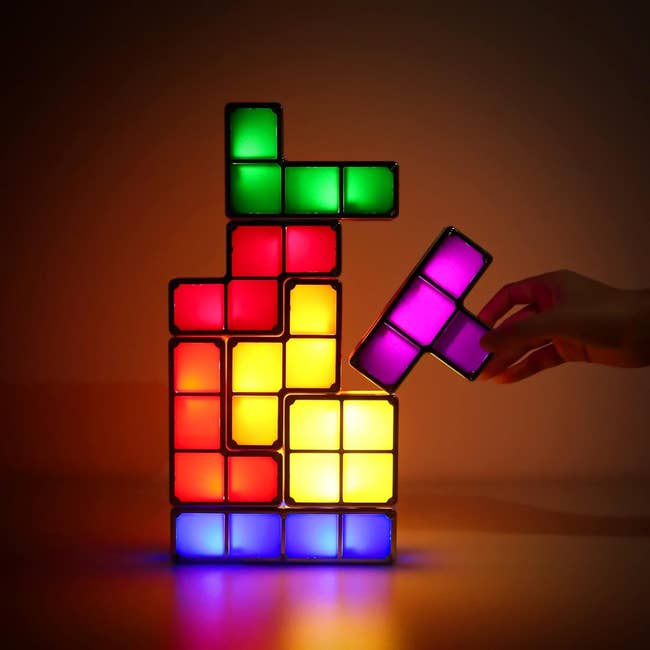 Mengatur tangan blok LED bergaya tetris berwarna-warni, membentuk tumpukan yang diterangi
