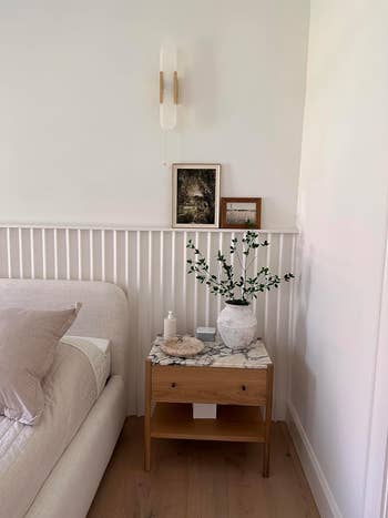 Side table with a vase of branches, adjacent to a sofa, showcasing a minimalist design suitable for modern interior shopping inspiration