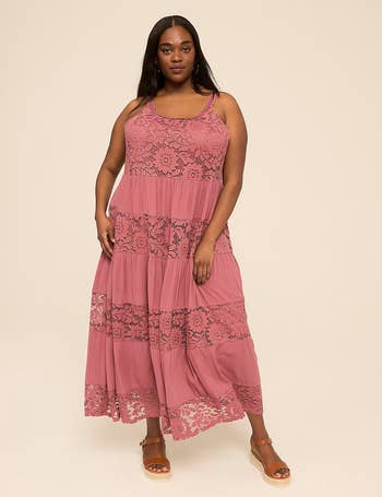 Woman wearing a sleeveless, tiered lace maxi formal  and wedge sandals, lasting  against a plain backdrop