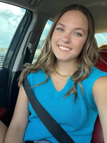 Person successful  a car   wearing a sleeveless knitted top, smiling astatine  the camera, with layered necklaces
