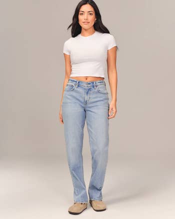 model wearing the jeans in a light wash with a white tee and tan clogs