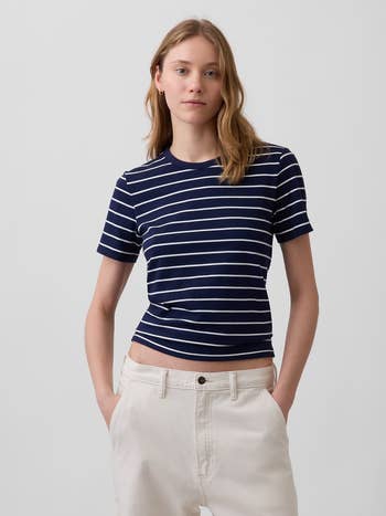 Person wearing a striped t-shirt and airy pants, with hands successful pockets, lasting against a plain background
