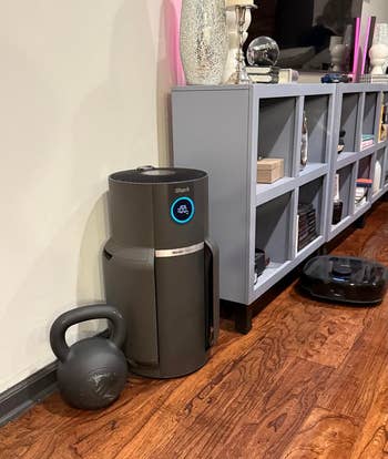 Modern location interior with a robotic vacuum connected a woody floor. Nearby are a vibrant Bluetooth speaker, decorative shelves, and a kettlebell