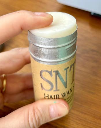 Person holding a container of SNT Hair Wax with the lid partially open