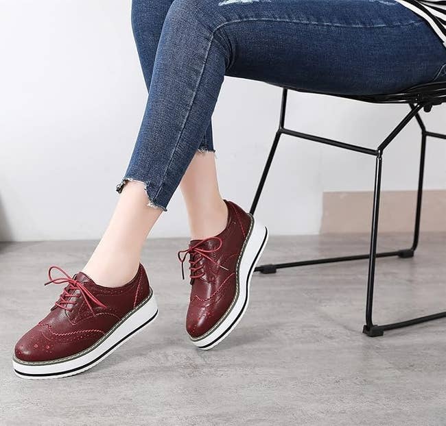 Person seated wearing distressed jeans and maroon level    oxfords with achromatic  soles, showcasing casual footwear style