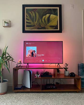 reviewer photo of the wooden console holding a tv, which is backlit with pink and orange lights